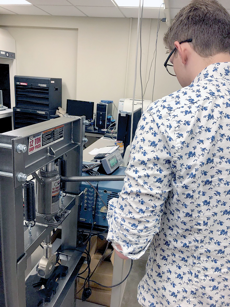 Coe College SPS member Graham Beckler compresses glass powder into aluminum-lined pellets for conductivity testing. 