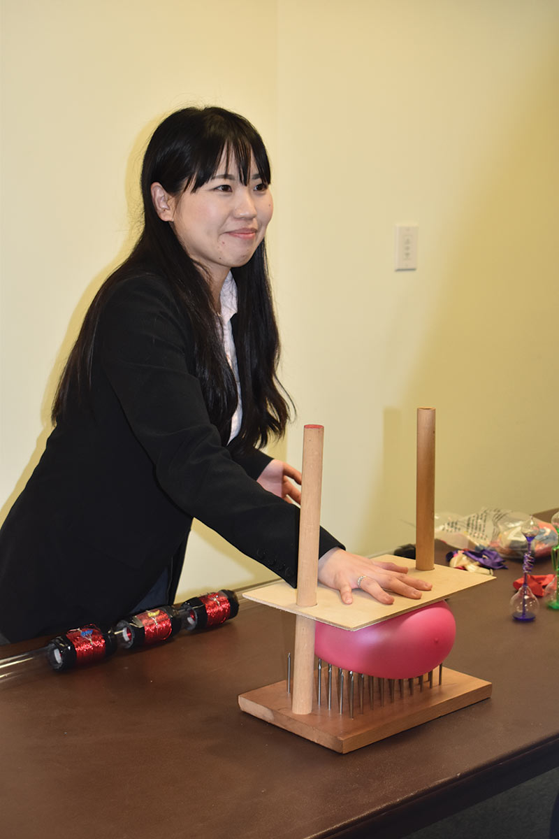 Assistant Professor Dr. Sachiko McBride demonstrates to students the concept of how pressure is the applied force divided by the area over which the force is exerted. The demo she made consisted of a bed of sharp nails with a simple latex balloon sandwiched between the nails and a safety plate. Students were amazed at the amount of force required to eventually pop the balloon.